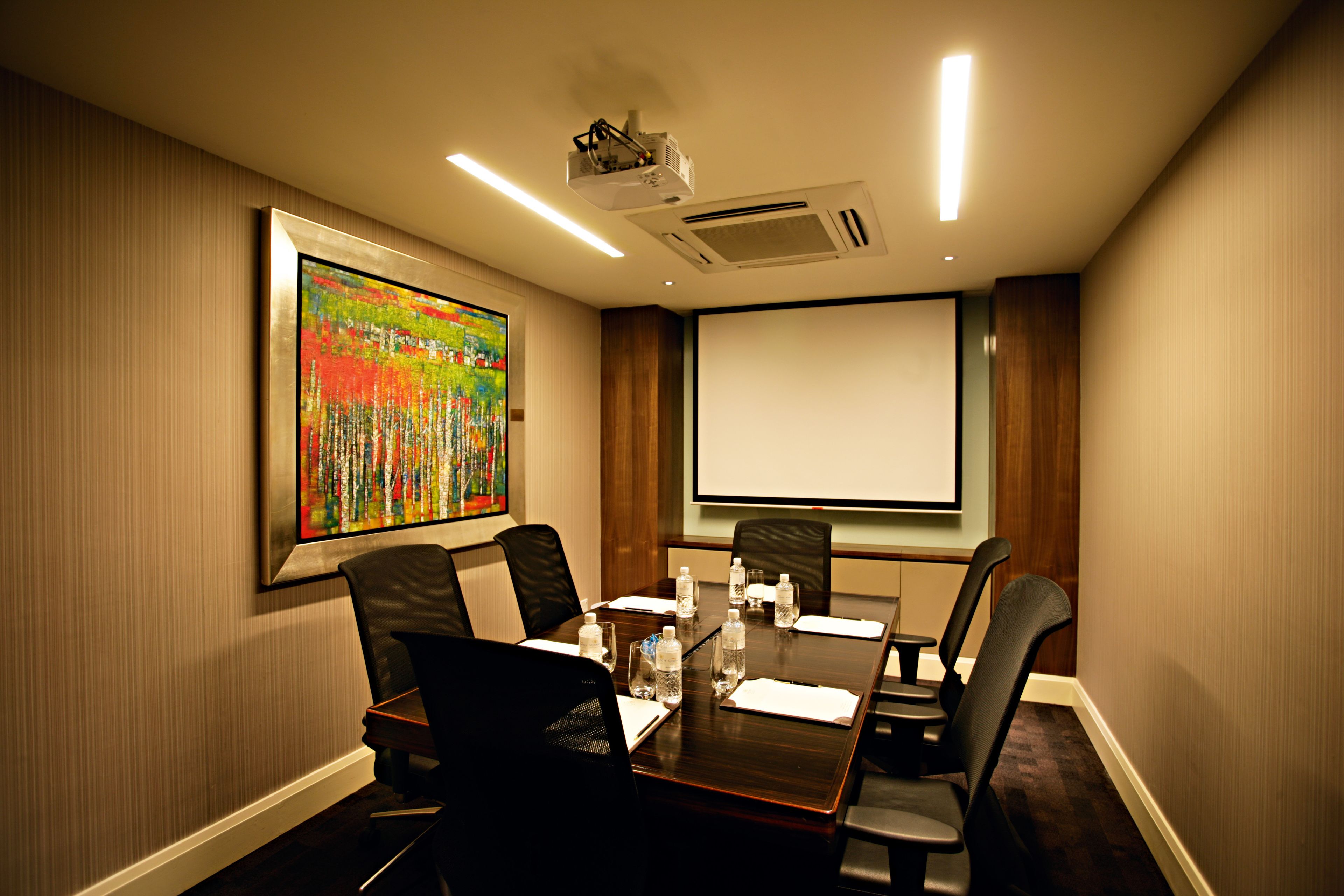 A conference room with a large table, chairs, a projector, and a screen.