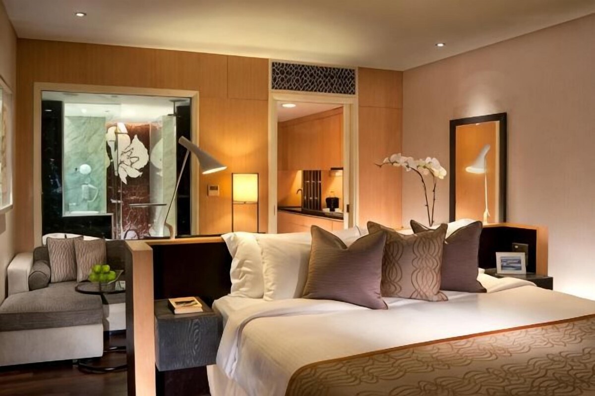 A hotel room with a bed, bedside table, lamp, chair, and a view of the interior.