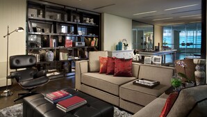 A modern living room with a sofa, a black leather chair, and a bookshelf filled with books and decorative items.