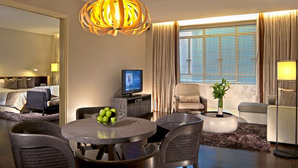 A hotel room with a dining area, a television, a plant, and a large window with curtains.