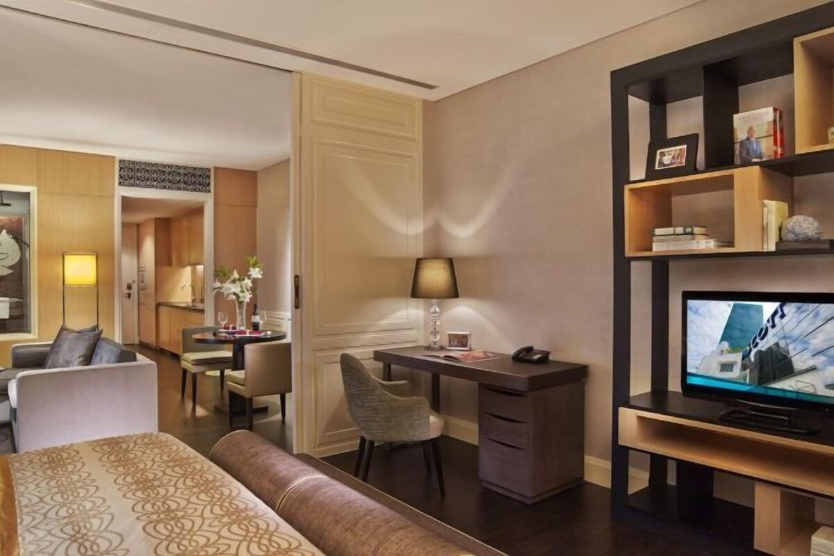 A hotel room with a bed, a desk, a chair, a television, and a bookshelf.