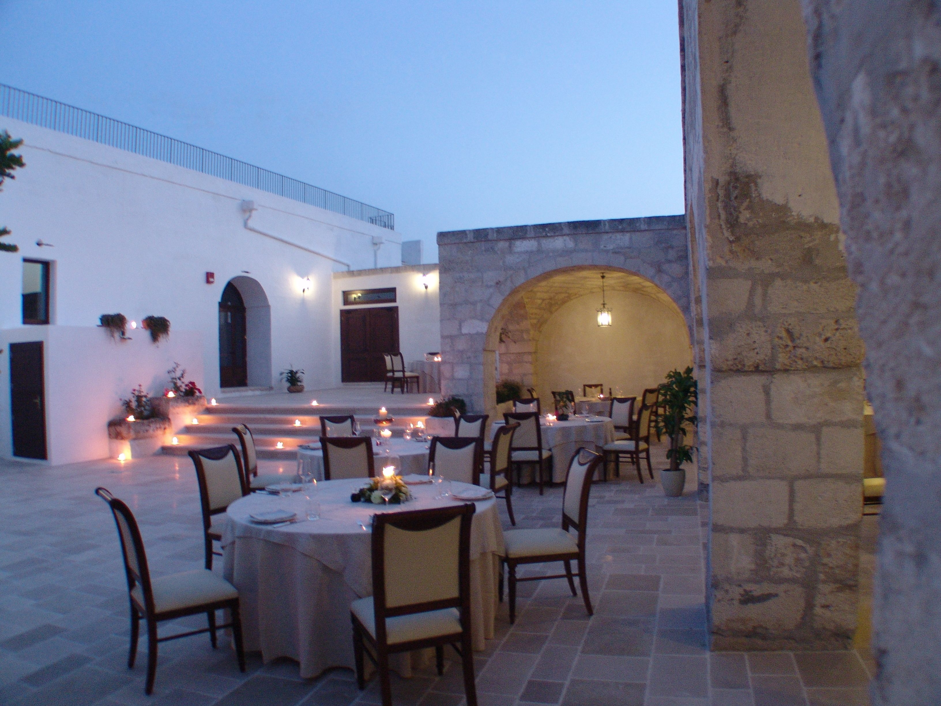 An outdoor dining area with round tables and chairs, stone walls, and a stone archway.