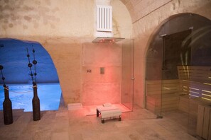 Una habitación con pared de piedra, puerta de cristal y una pequeña banca.