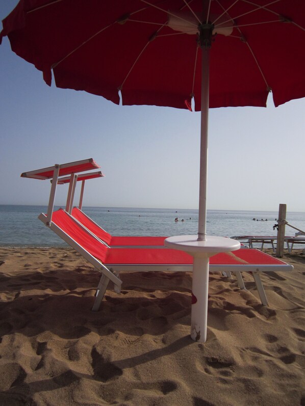 Une plage avec des chaises longues rouges et blanches et un parasol rouge.