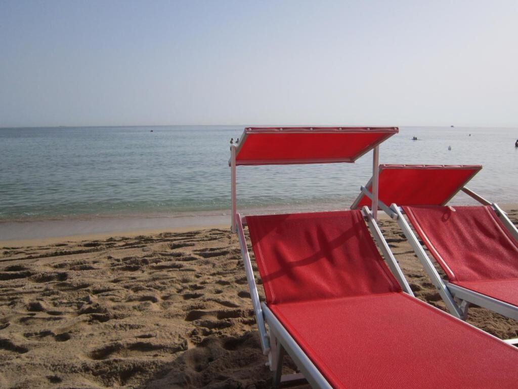 Two red beach chairs with metal frames on a sandy beach, facing the ocean.
