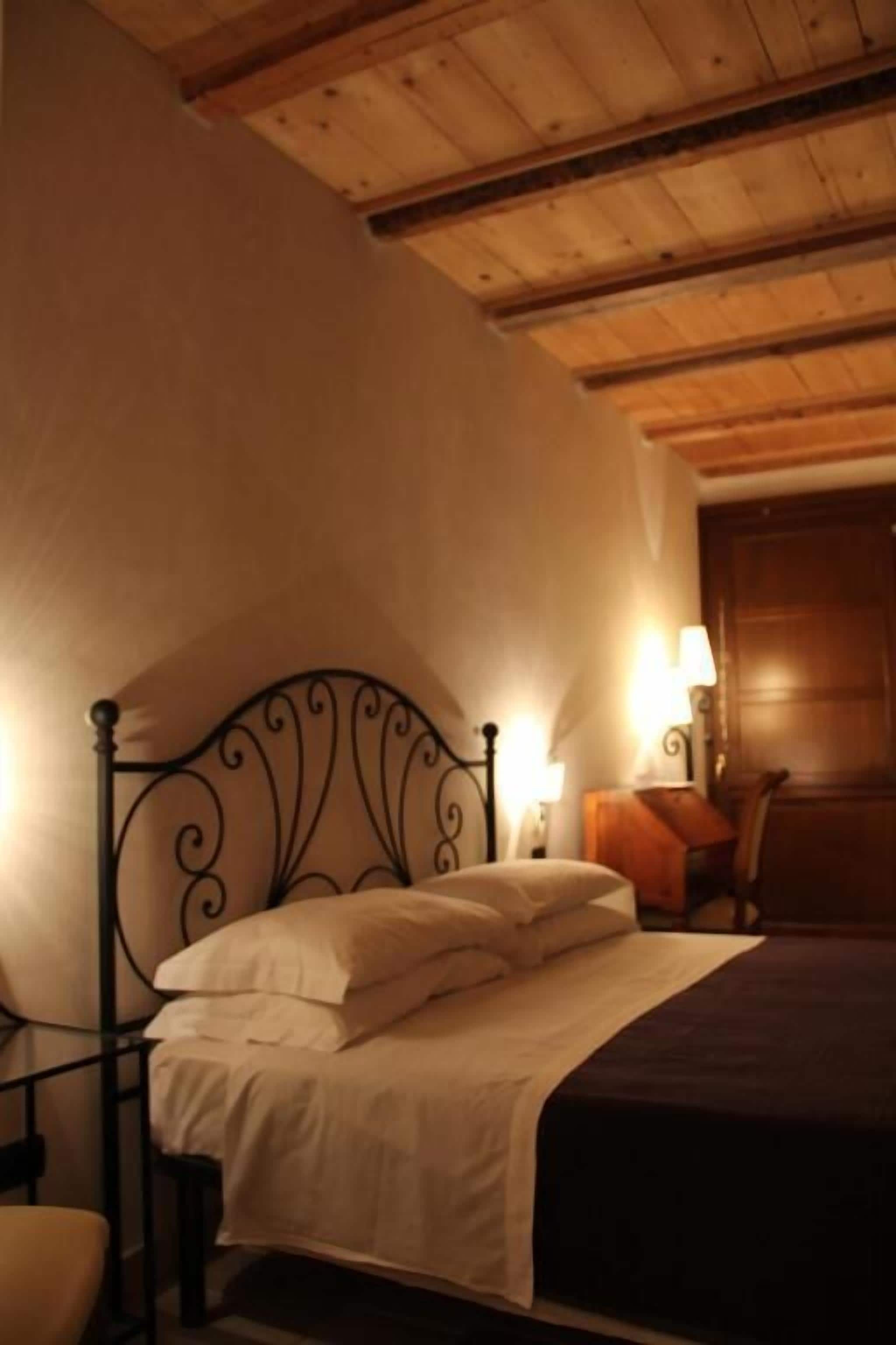 Un dormitorio con techo de madera, estructura de cama de metal, mesita de noche con lámpara y una silla.
