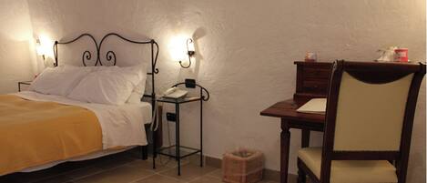 A bedroom with a bed, bedside table with a phone, a chair, and a small table with a lamp.