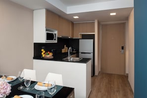 Cocina moderna con microondas, lavamanos y refrigerador. Hay una zona de comedor con una mesa preparada para dos personas, y una puerta que da a otra habitación.