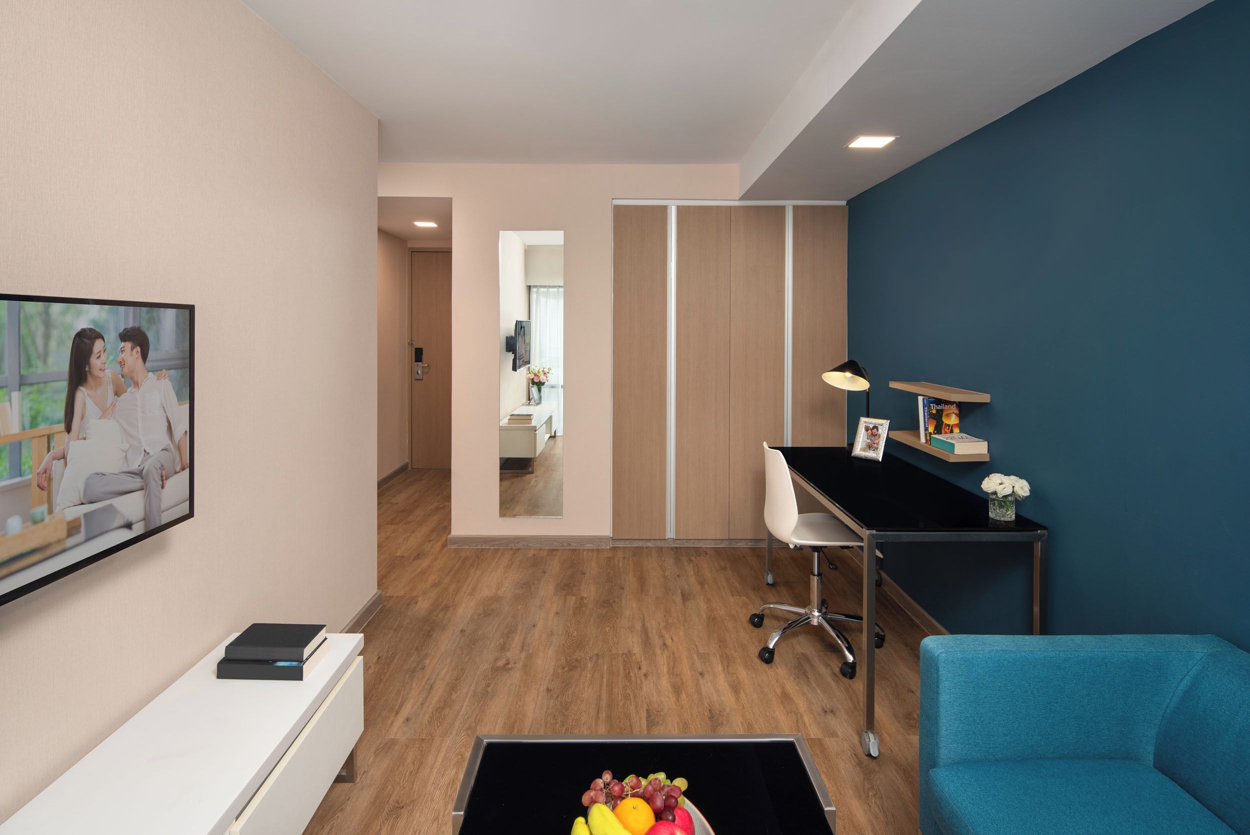 Une chambre moderne équipée d’une télévision, d’un bureau, d’une chaise et d’une table basse sur laquelle se trouvent des fruits.