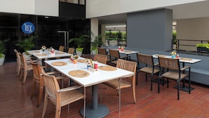 An outdoor dining area with multiple tables and chairs, some with placemats and cutlery.