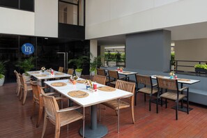 Uma área de refeições ao ar livre com várias mesas e cadeiras, algumas com jogos de mesa e talheres.