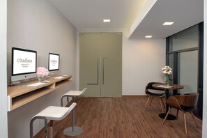A modern reception area with two monitors, a reception desk, a waiting area with chairs, and a small table with a vase of flowers. - Citadines Sukhumvit 8 Bangkok (Bangkok)