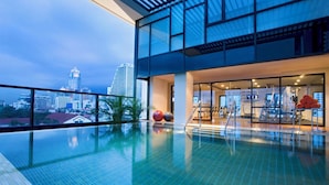 A rooftop swimming pool with a city view, indoor gym, and exercise equipment.