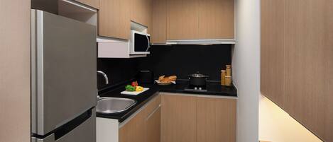Cocina compacta con refrigerador, microondas, pileta y muebles de madera.