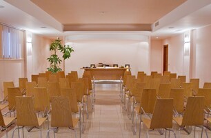 Ein Konferenzraum mit Reihen aus Holzsesseln, einem Rednerpult und einem Blumentopf.