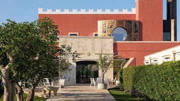 Ein Gebäude mit roter Fassade, steinernen Haupteingang und Außenbestuhlung.