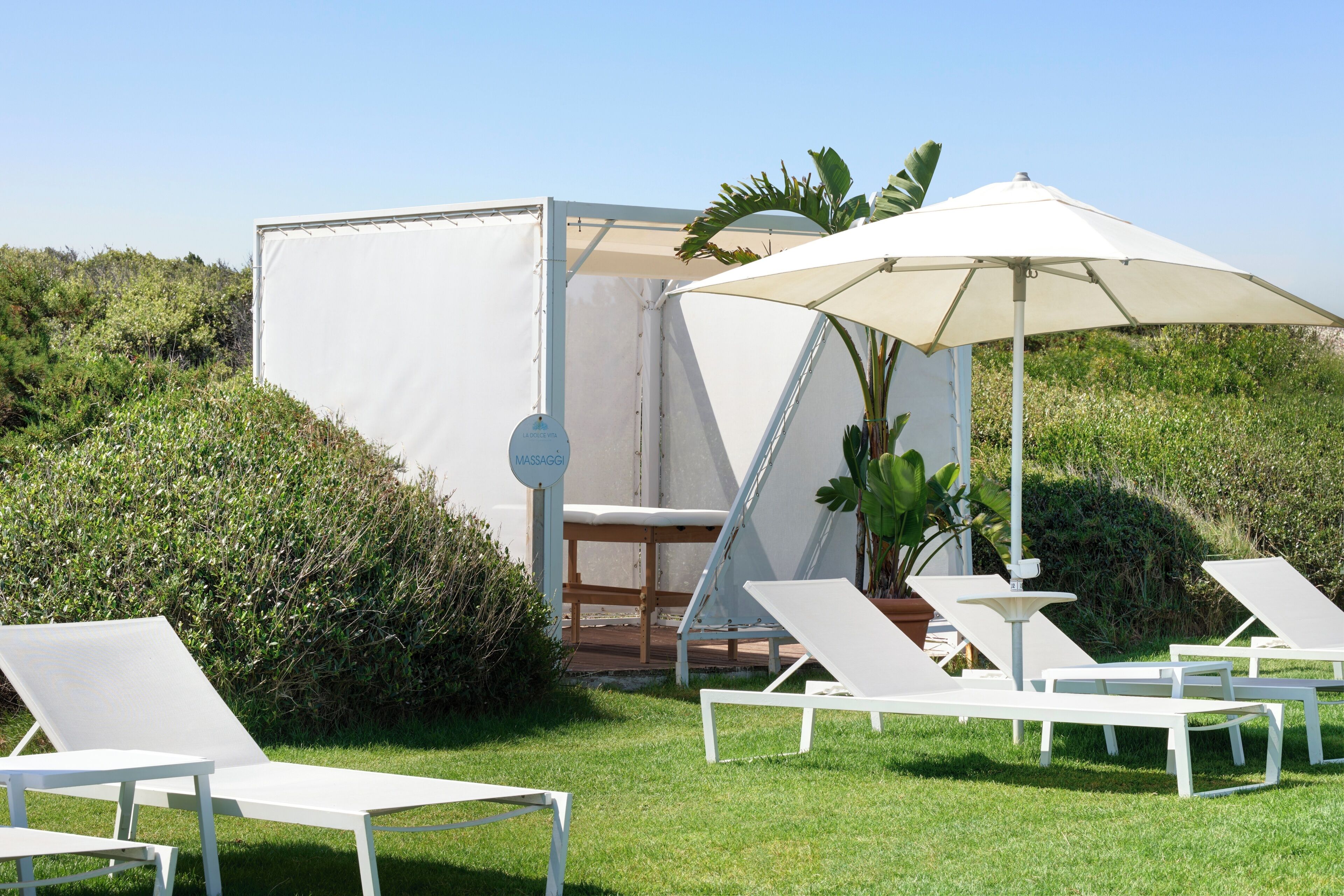 Un espacio exterior con asientos blancos, sillones reclinables y una sombrilla.
