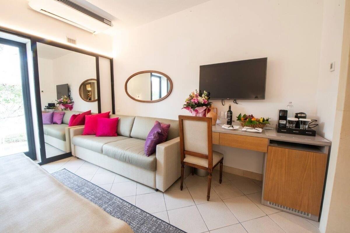 Een moderne woonkamer met een bank, een houten stoel, een bureau met een koffiezetapparaat en een televisie aan de muur.