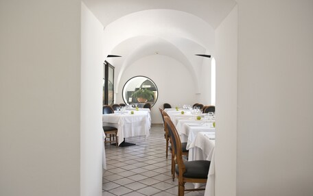 A dining area with white tables and chairs, a tiled floor, and a large circular window.