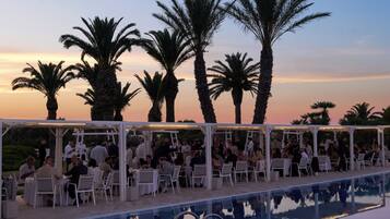An outdoor pool area with white canopied seating and palm trees in the background.