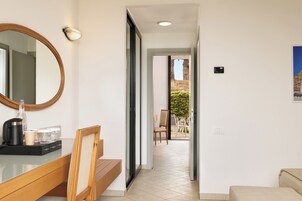 A hotel room with a wooden bench, a mirror, a coffee maker, and a view of the outside.
