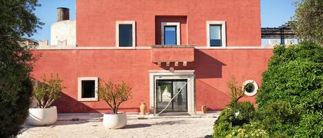 A red building with a central entrance, two windows on the upper floor, and a balcony.