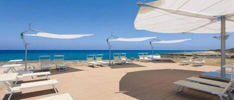 Um terraço à beira-mar com espreguiçadeiras e guarda-sóis, com vista para o oceano.