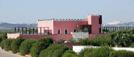 A pink building with a castle-like structure, surrounded by well-maintained greenery and a clear view of a distant cityscape.