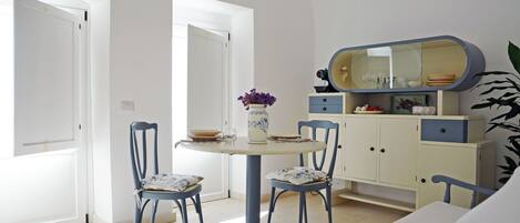 A dining area with a round table, two chairs, a vase with flowers, and a cabinet with a mirror.