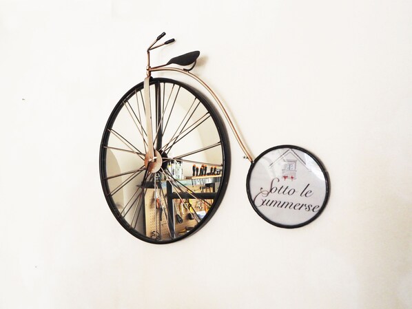 A wall-mounted bicycle with a mirror reflecting a room and a circular sign with text. - Sotto Le Cummerse Albergo Diffuso (Locorotondo)