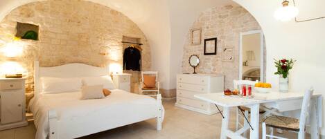A bedroom with a stone wall, a bed, a dresser, a vanity, and a table with a chair.