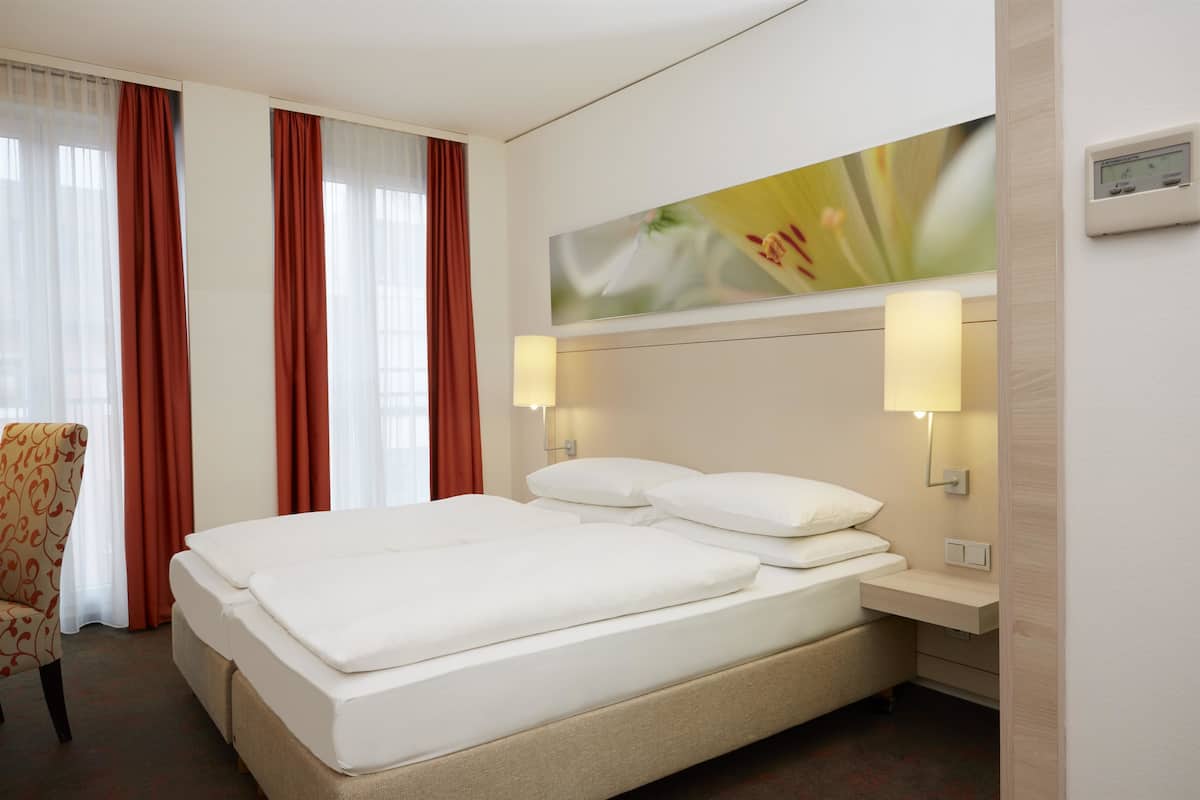 A hotel room with a large bed, two bedside tables, a chair, and a wall-mounted light fixture.
