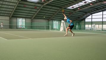 Una cancha de tenis interior con red, un jugador en movimiento y una escalera.