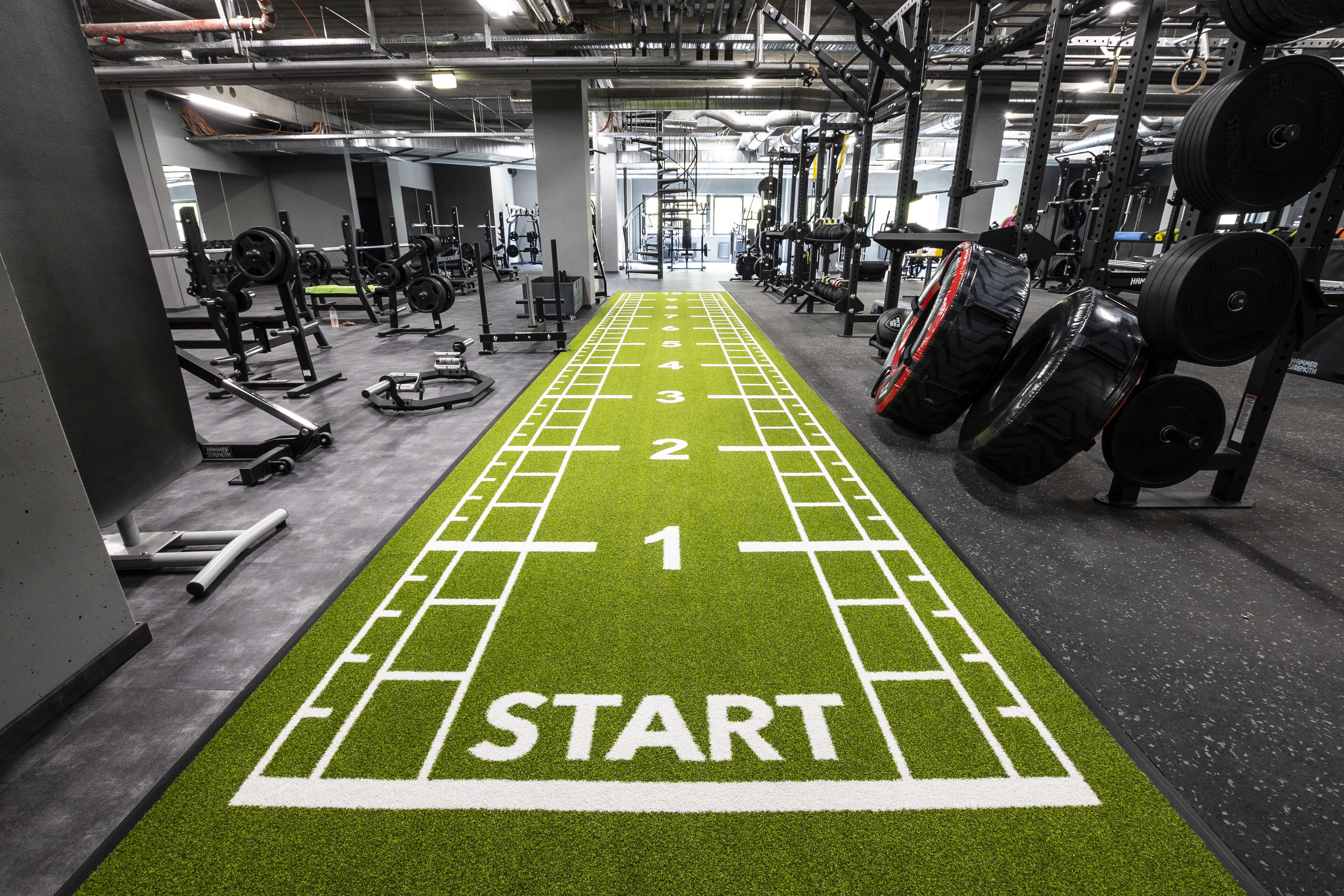 Un gimnasio con una pista de atletismo verde marcada con números y un cartel que dice 'START'.