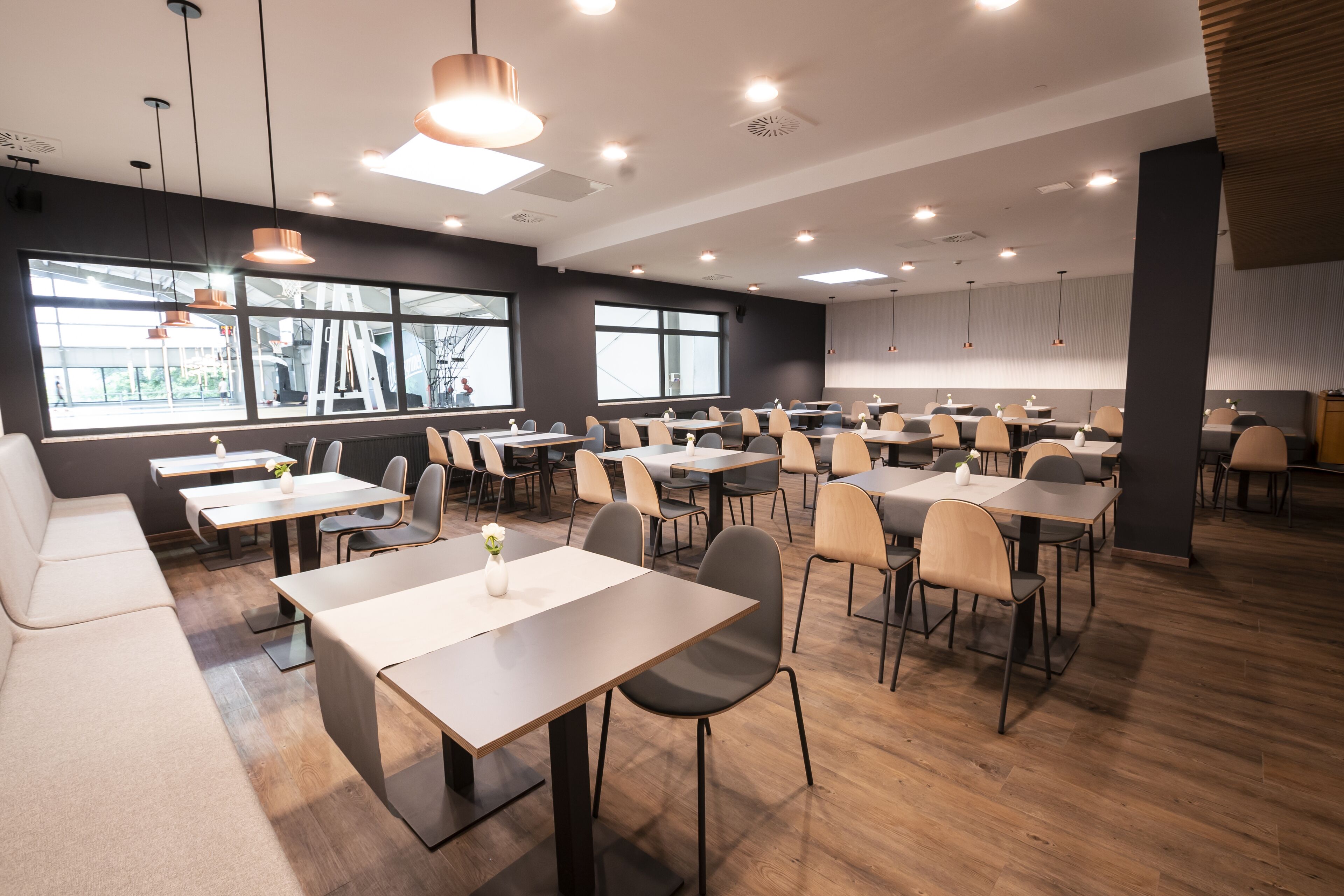 A modern dining area with multiple tables and chairs, large windows, and pendant lighting.
