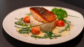Un plato de comida con un trozo de pescado sobre arroz, adornado con vegetales y tomates cherry.