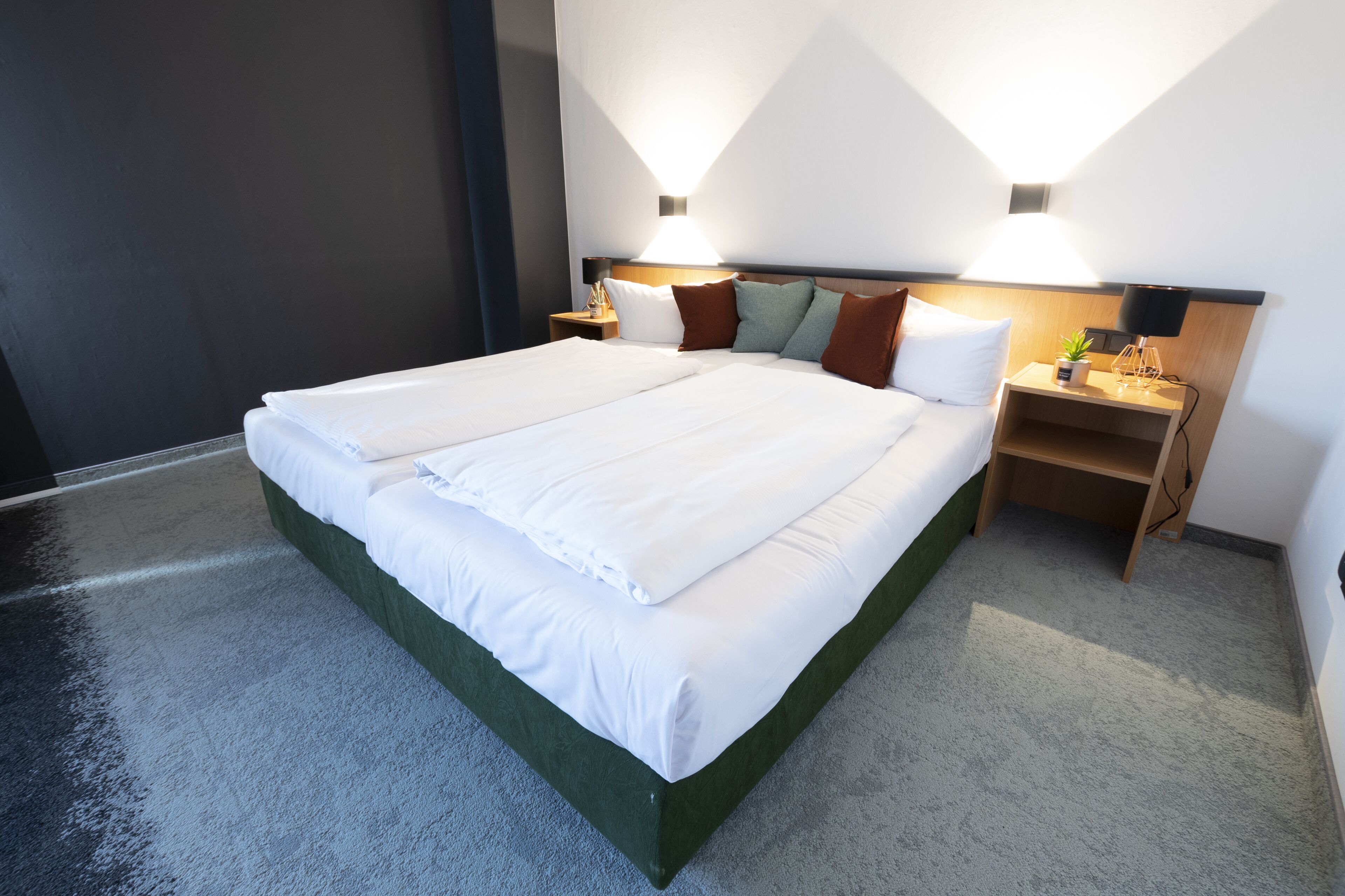 A modern hotel room with a large bed, two bedside tables, and wall-mounted lighting.