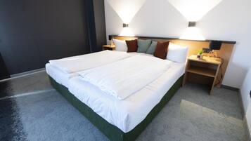 A modern hotel room with a large bed, two bedside tables, and wall-mounted lighting.