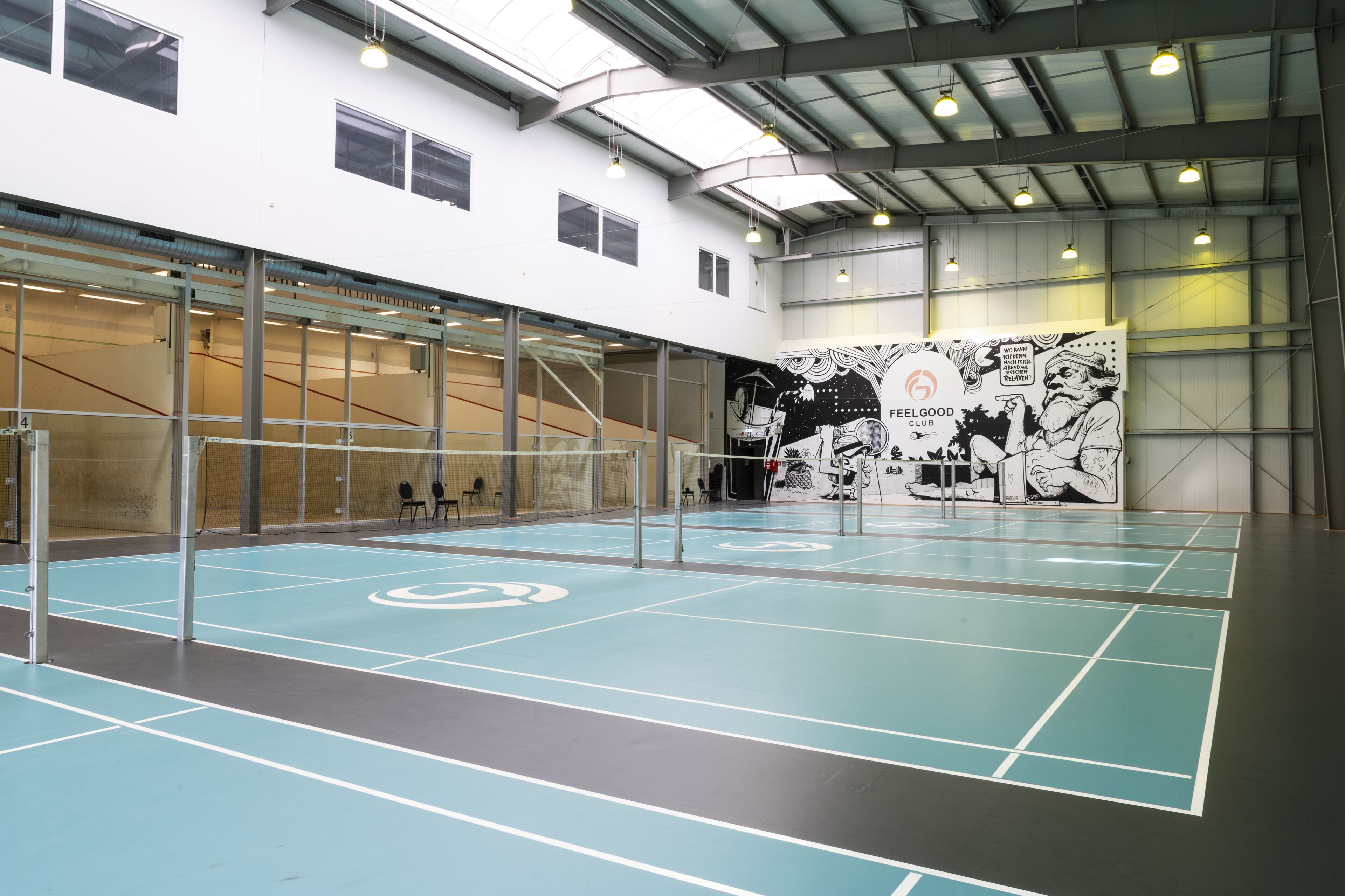 Instalación deportiva interior con una cancha de voleibol, paredes de vidrio y un mural.