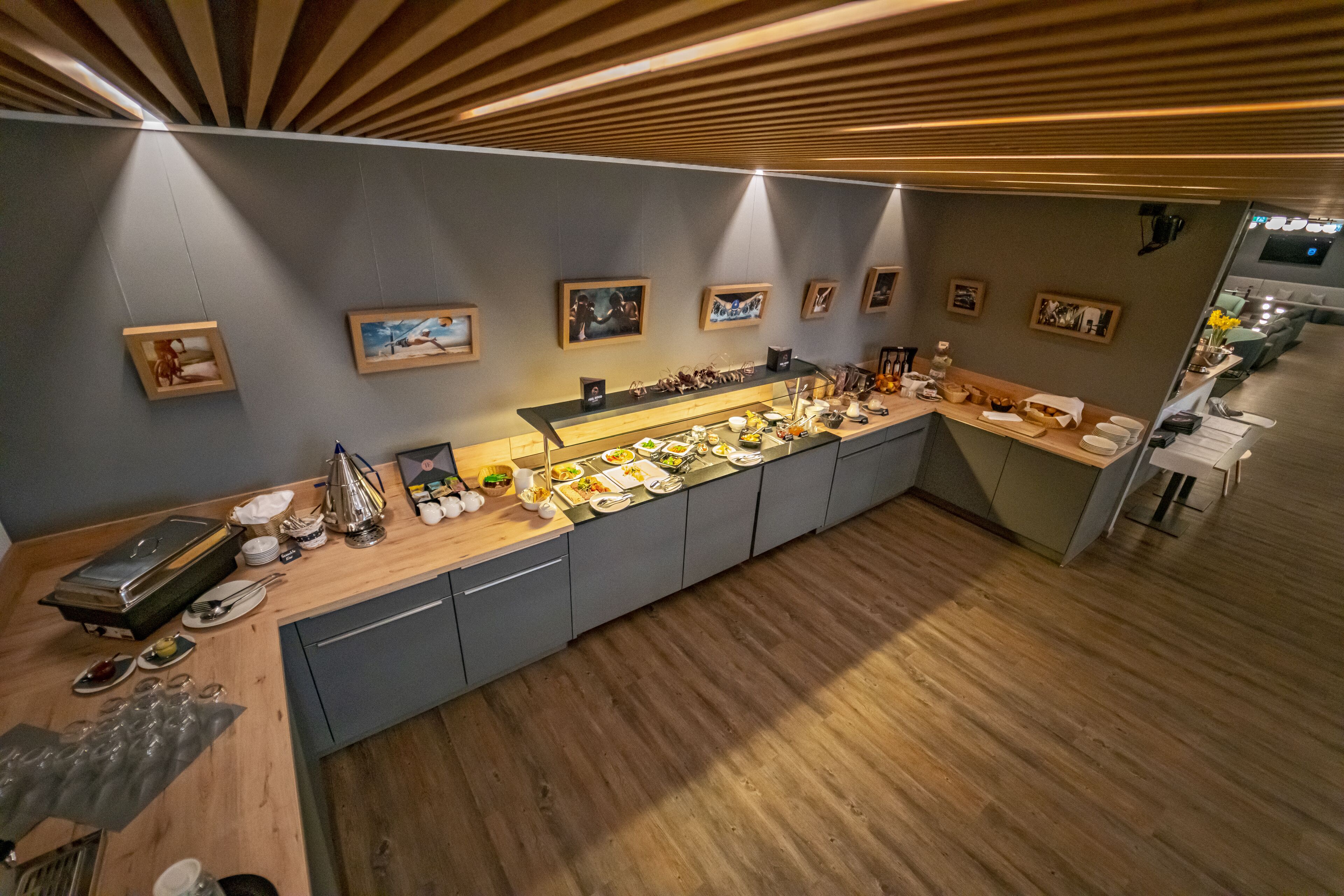 A modern kitchen with a long counter, wooden ceiling, and framed pictures on the wall.