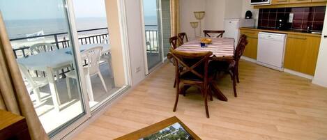 Un balcón con vista al mar, un comedor con mesa y sillas, y una cocina con muebles de madera y lavavajillas.