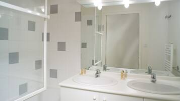 A bathroom with two sinks, a large mirror, and a glass shower enclosure.
