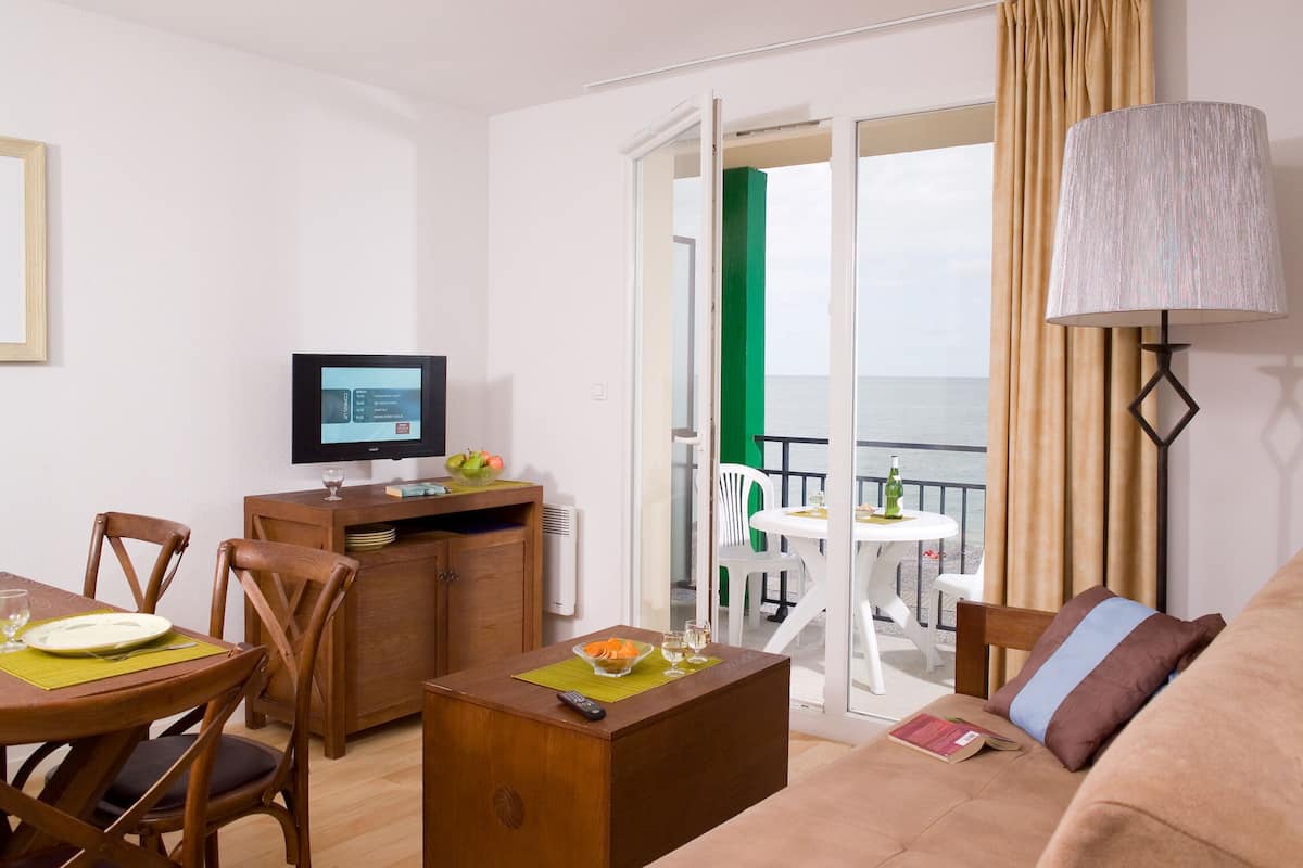 Ein Zimmer mit Esstisch, Stühlen, einer Couch, einem Fernseher und einem Balkon mit Meerblick.