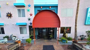 Um edifício com toldo vermelho, uma fonte e uma estátua no pátio.