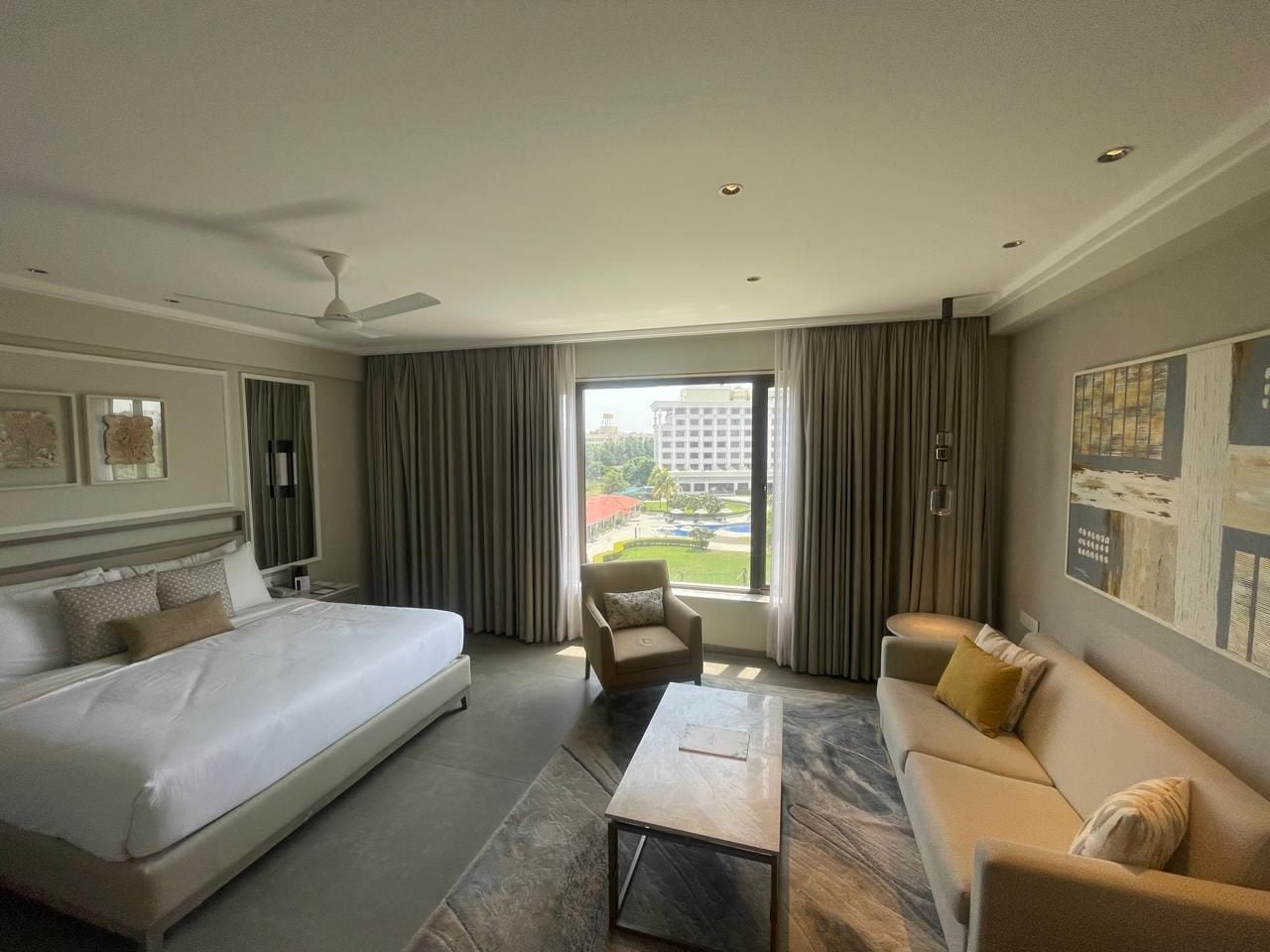 A hotel room with a large bed, a sofa, a chair, and a view of a building through the window.