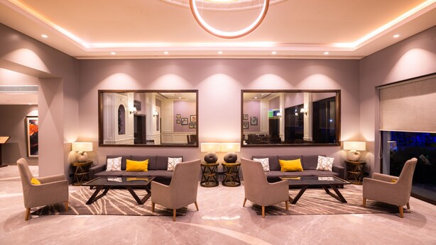 A modern hotel lobby with a central seating area, large mirrors, and ambient lighting. - Sun N Sand Shirdi (Rahata)