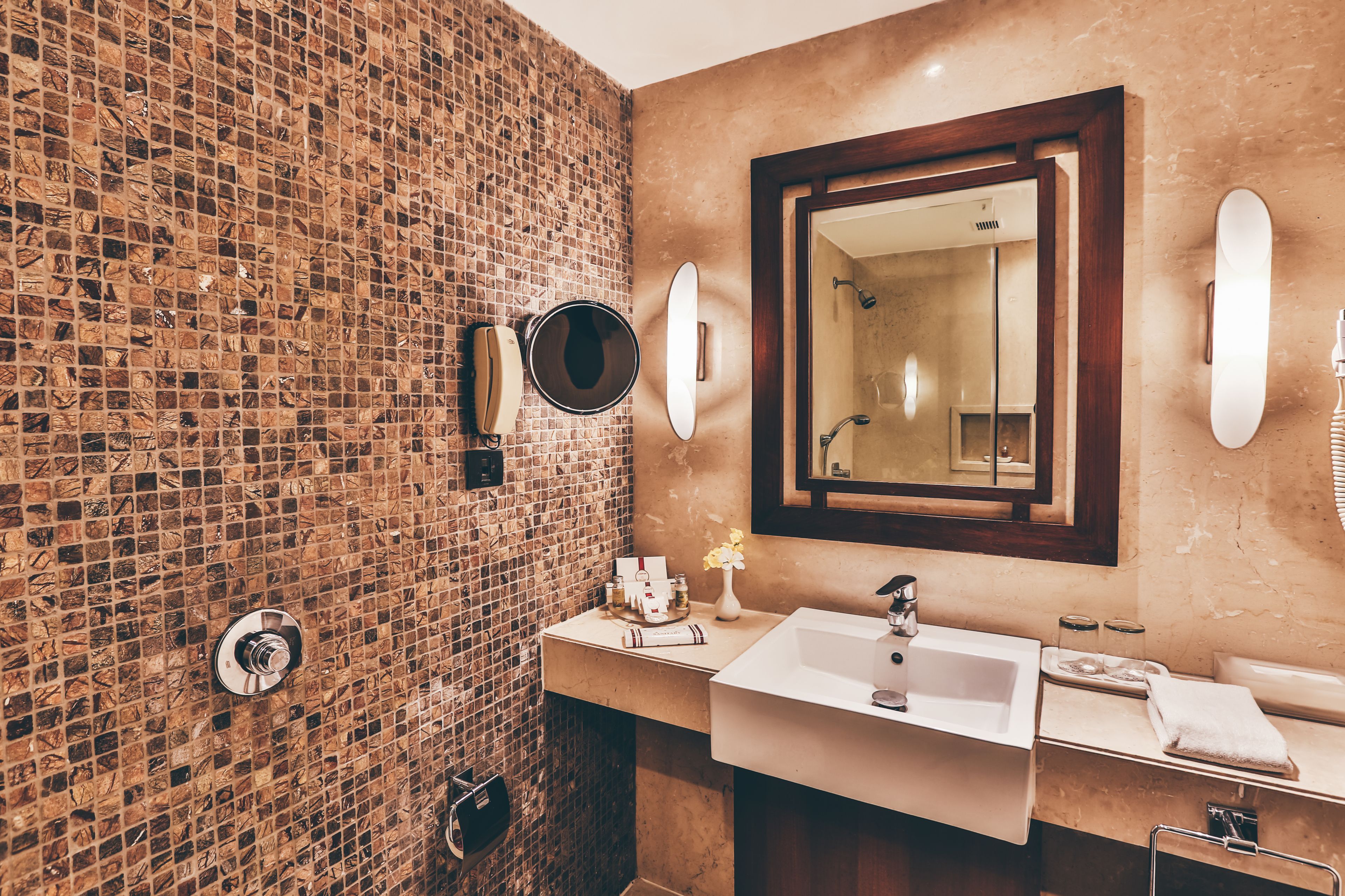Un baño con pared de ladrillo, un espejo grande, un lavamanos y un perchero para toallas.