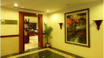 A hotel lobby with a marble floor, a large abstract painting, and a potted plant.