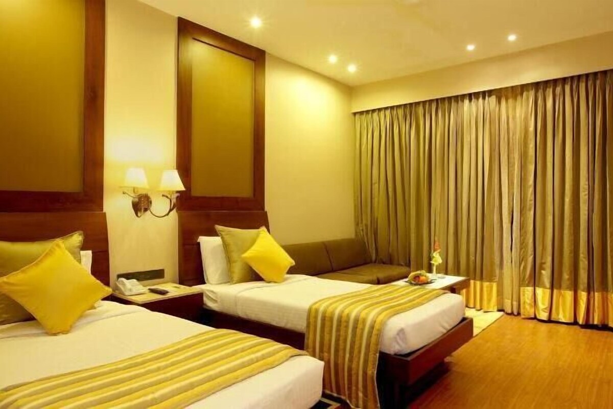 A hotel room with two beds, a nightstand with a lamp, a mirror, and a window with curtains.