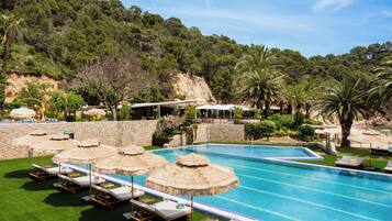 A swimming pool with lounge chairs and umbrellas, surrounded by greenery and a stone wall.